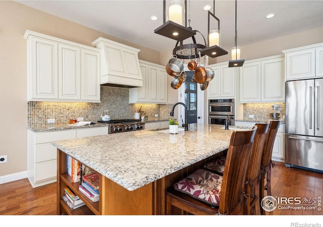 kitchen with stainless steel appliances, white cabinetry, light stone countertops, and a center island with sink