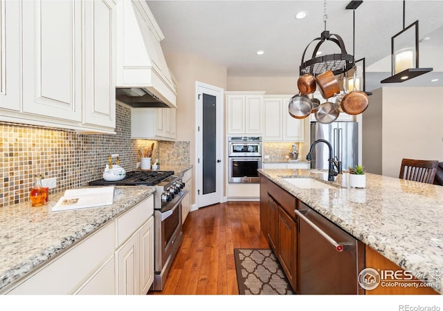 kitchen featuring premium range hood, pendant lighting, sink, white cabinets, and stainless steel appliances