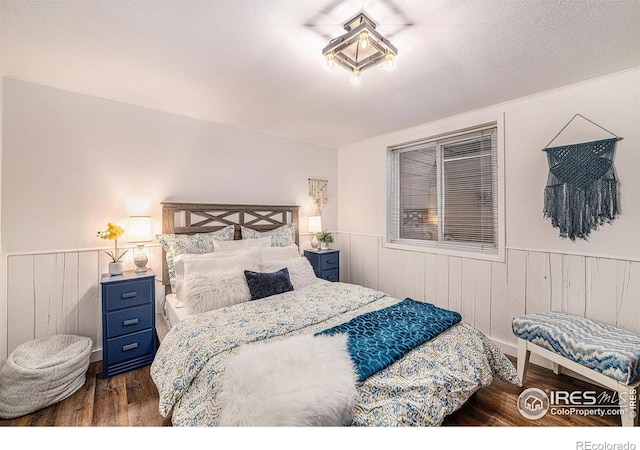 bedroom with a textured ceiling, dark wood-type flooring, and wainscoting