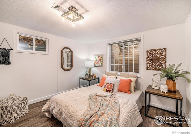 bedroom featuring visible vents, baseboards, a textured ceiling, and wood finished floors