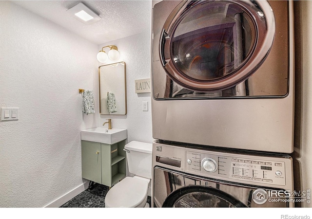 half bathroom with vanity, a textured wall, and stacked washing maching and dryer