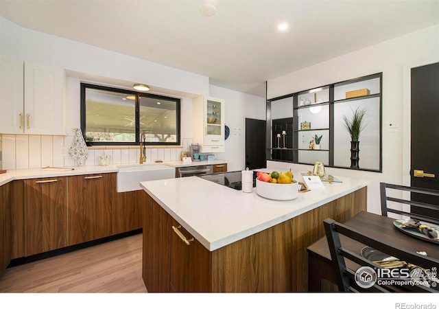 kitchen featuring a sink, backsplash, white cabinets, and light countertops