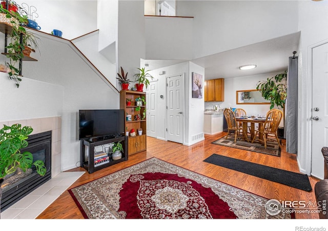 living room with a towering ceiling, a tiled fireplace, and light wood-type flooring