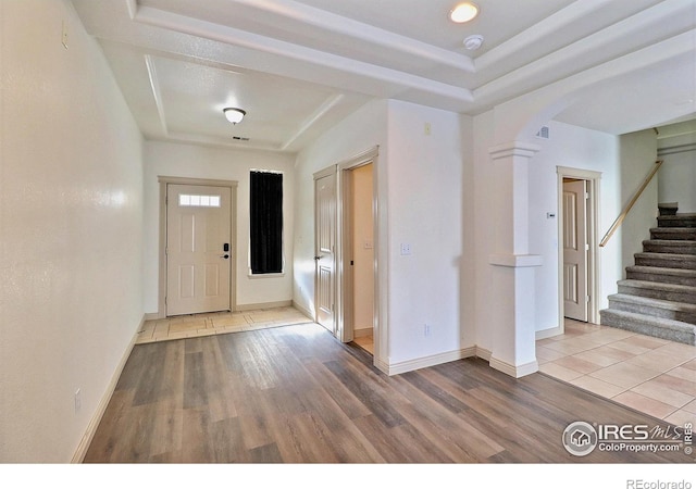 entryway with wood-type flooring, a raised ceiling, and ornate columns