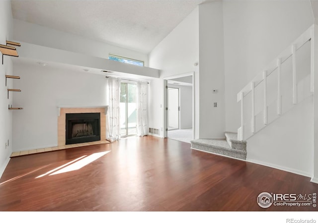 unfurnished living room with a tile fireplace, wood-type flooring, a textured ceiling, and high vaulted ceiling