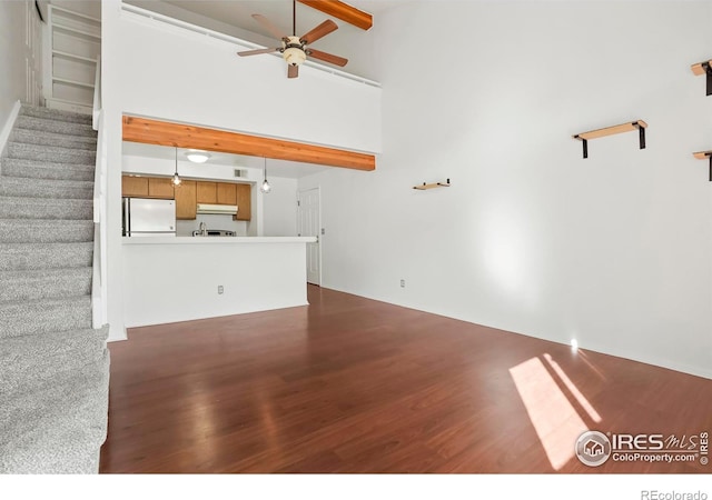 unfurnished living room featuring beam ceiling, dark wood-type flooring, ceiling fan, and a towering ceiling