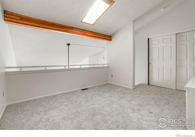 interior space featuring light carpet, vaulted ceiling with beams, and a textured ceiling