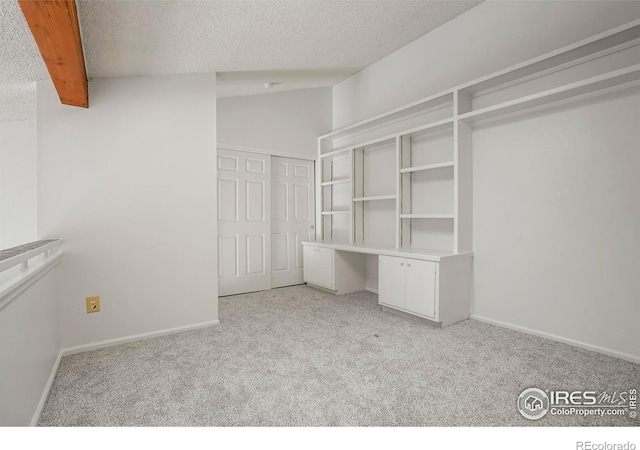 walk in closet featuring light colored carpet, built in desk, and vaulted ceiling