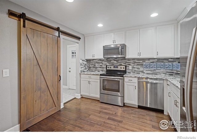 kitchen featuring white cabinetry, backsplash, stainless steel appliances, light stone countertops, and a barn door