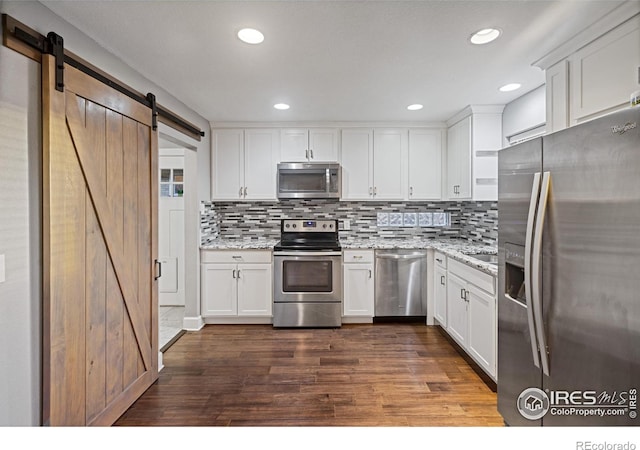 kitchen with stainless steel appliances, white cabinetry, a barn door, and light stone counters