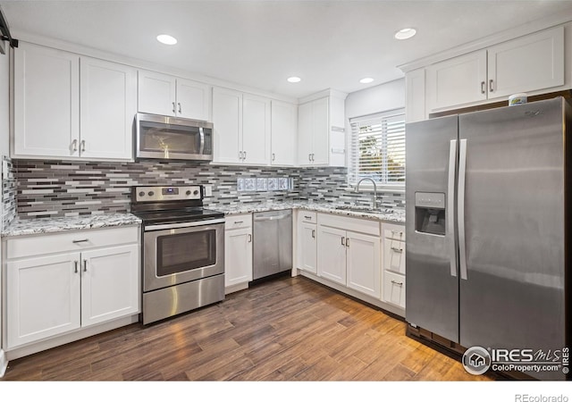 kitchen with sink, stainless steel appliances, dark hardwood / wood-style floors, light stone countertops, and white cabinets