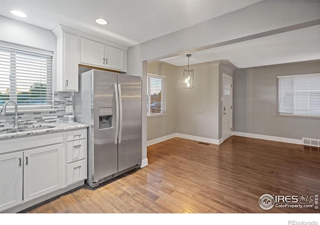 kitchen with stainless steel refrigerator with ice dispenser, sink, light wood-type flooring, light stone countertops, and white cabinets