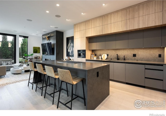 kitchen with a breakfast bar, sink, tasteful backsplash, a large island, and light hardwood / wood-style floors