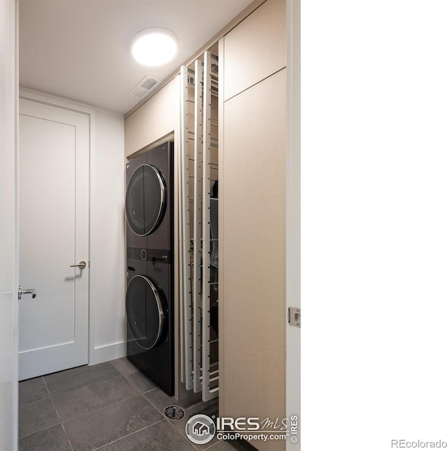 washroom with stacked washer and clothes dryer and dark tile patterned flooring