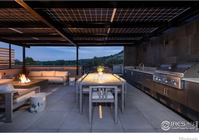 patio terrace at dusk featuring sink, area for grilling, and an outdoor living space with a fire pit