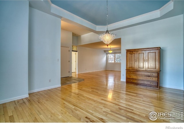 spare room with a raised ceiling, ornamental molding, a chandelier, and light hardwood / wood-style floors