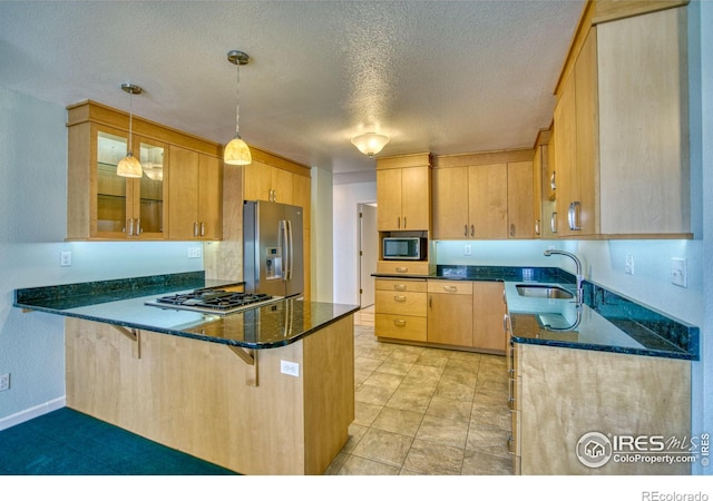 kitchen featuring sink, appliances with stainless steel finishes, hanging light fixtures, kitchen peninsula, and dark stone counters