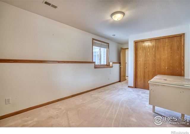 unfurnished bedroom with light colored carpet, a closet, and a textured ceiling