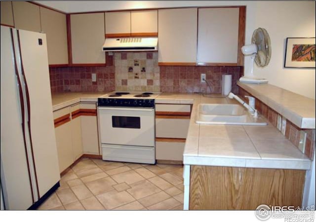 kitchen featuring sink, white appliances, light tile patterned floors, tasteful backsplash, and tile counters