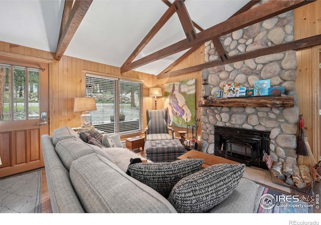 living room with a stone fireplace, beamed ceiling, a healthy amount of sunlight, and wood walls