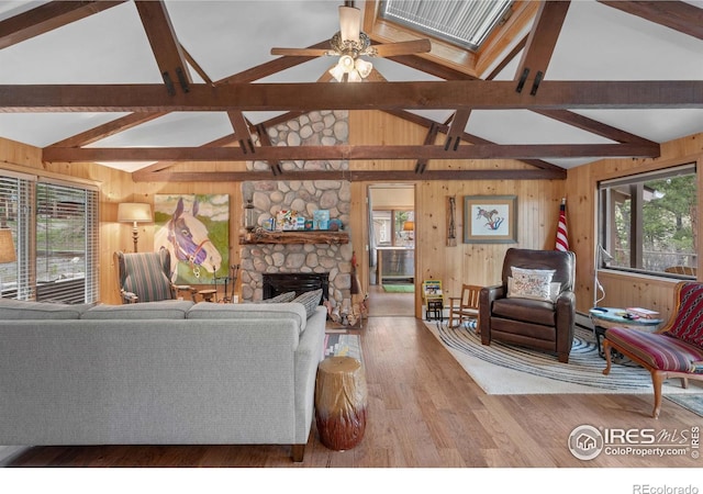 living room featuring vaulted ceiling with beams, wooden walls, ceiling fan, a fireplace, and hardwood / wood-style floors