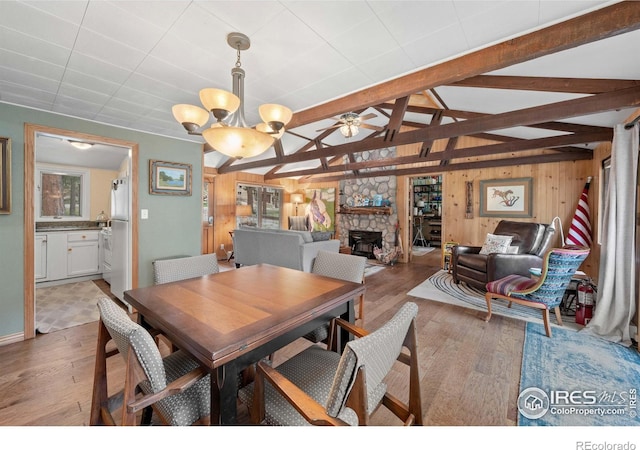 dining room featuring lofted ceiling with beams, a fireplace, light wood-type flooring, and wood walls