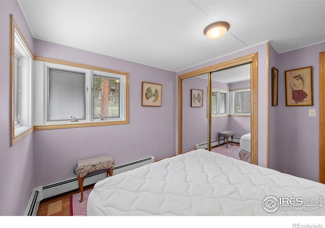 bedroom featuring multiple windows, hardwood / wood-style floors, a closet, and baseboard heating