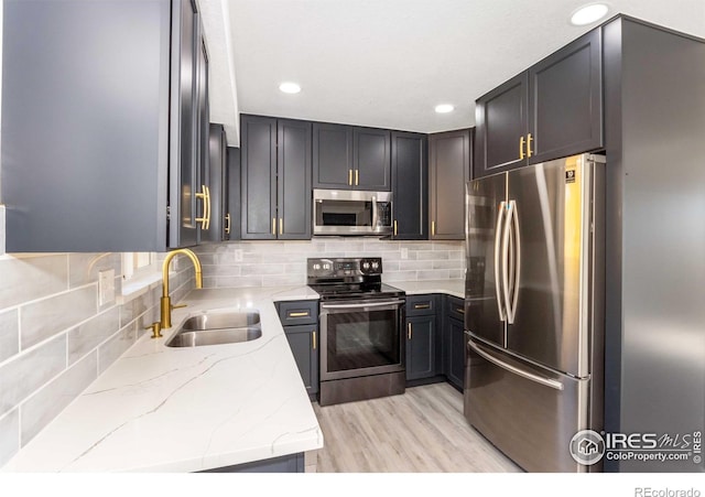 kitchen featuring sink, backsplash, stainless steel appliances, light stone countertops, and light hardwood / wood-style flooring