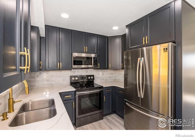 kitchen featuring sink, light stone counters, stainless steel appliances, light hardwood / wood-style floors, and decorative backsplash