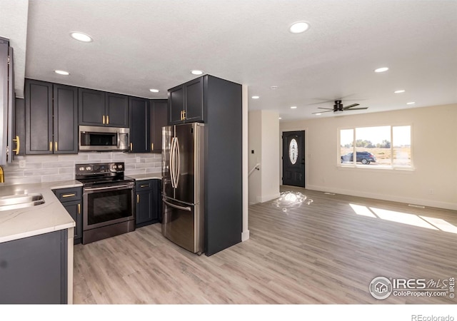 kitchen featuring sink, stainless steel appliances, tasteful backsplash, light stone counters, and light wood-type flooring