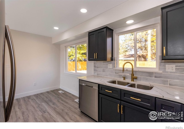 kitchen with sink, decorative backsplash, light hardwood / wood-style floors, light stone counters, and stainless steel appliances