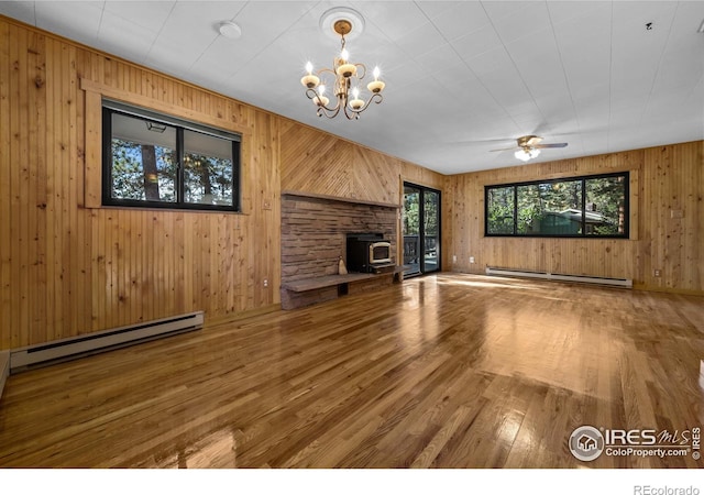 unfurnished living room with a baseboard heating unit, hardwood / wood-style flooring, ceiling fan with notable chandelier, and a wood stove