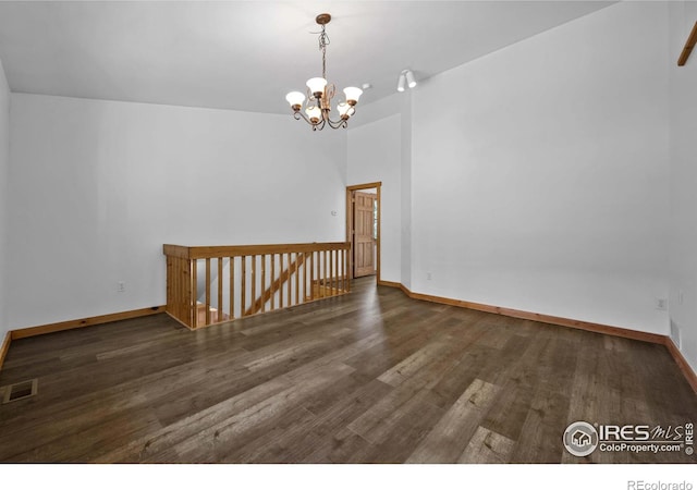 empty room with a notable chandelier and dark wood-type flooring