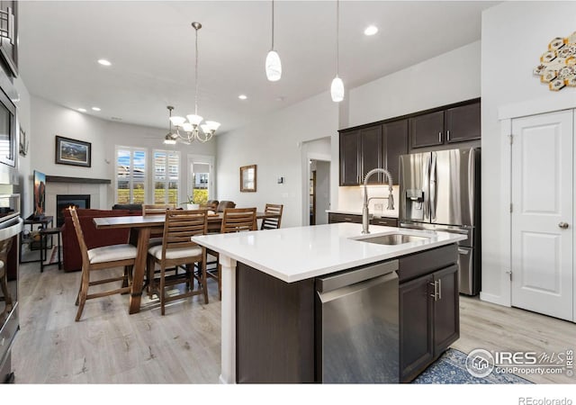 kitchen with sink, hanging light fixtures, stainless steel appliances, dark brown cabinets, and a center island with sink