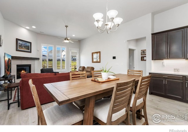 dining space featuring ceiling fan with notable chandelier, a tile fireplace, and light wood-type flooring