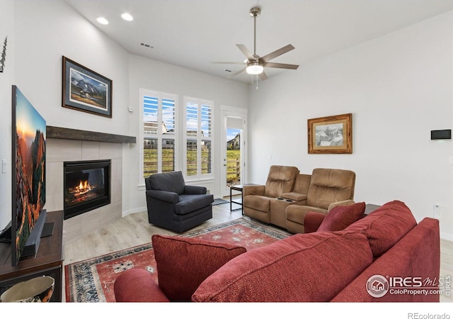 living room featuring ceiling fan, a tiled fireplace, and light hardwood / wood-style flooring