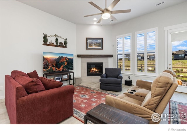 living room featuring a tiled fireplace, ceiling fan, and light hardwood / wood-style floors