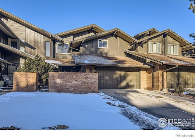 view of front of house with driveway, an attached garage, board and batten siding, and brick siding