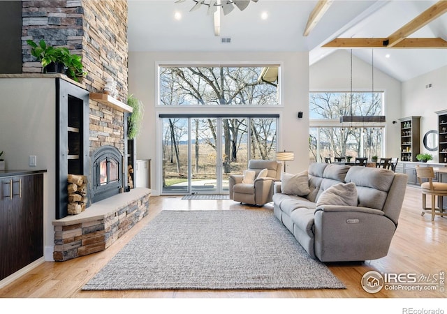 living room with a stone fireplace, high vaulted ceiling, light wood-type flooring, beamed ceiling, and ceiling fan