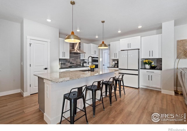 kitchen with appliances with stainless steel finishes, white cabinetry, hanging light fixtures, light stone countertops, and a center island with sink