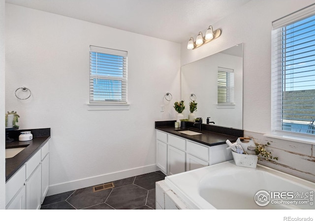 bathroom with tile patterned flooring, vanity, a healthy amount of sunlight, and a tub to relax in