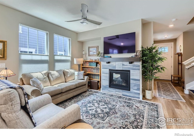 living room featuring ceiling fan, plenty of natural light, a tiled fireplace, and light hardwood / wood-style floors