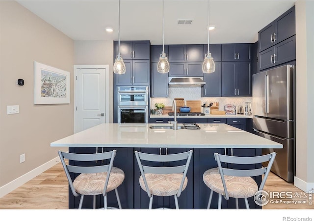 kitchen with a center island with sink, a kitchen breakfast bar, stainless steel appliances, light stone countertops, and backsplash