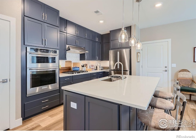 kitchen featuring a breakfast bar, an island with sink, pendant lighting, stainless steel appliances, and light hardwood / wood-style floors