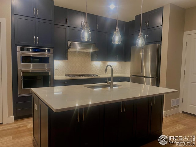 kitchen with pendant lighting, sink, stainless steel appliances, light stone countertops, and a center island with sink