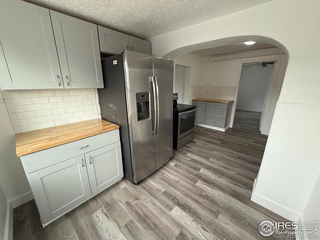 kitchen featuring appliances with stainless steel finishes, backsplash, a textured ceiling, wood counters, and light wood-type flooring