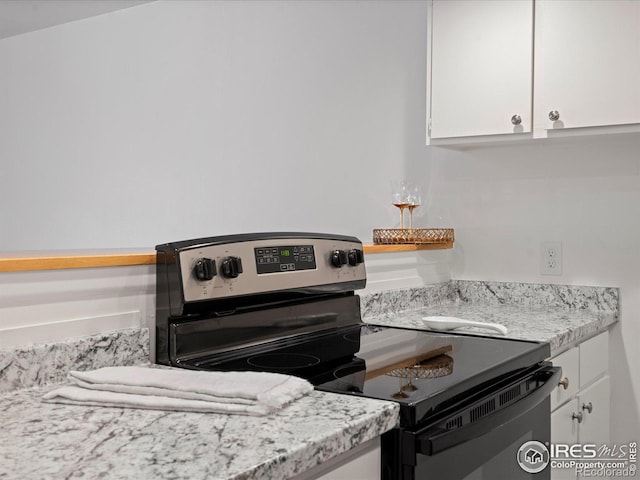 kitchen with light stone countertops, stainless steel electric range, and white cabinets