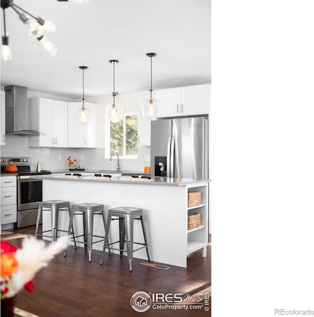 kitchen featuring wall chimney range hood, a breakfast bar, appliances with stainless steel finishes, white cabinetry, and hanging light fixtures