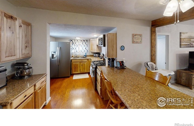 kitchen featuring sink, light hardwood / wood-style flooring, a textured ceiling, appliances with stainless steel finishes, and light stone countertops