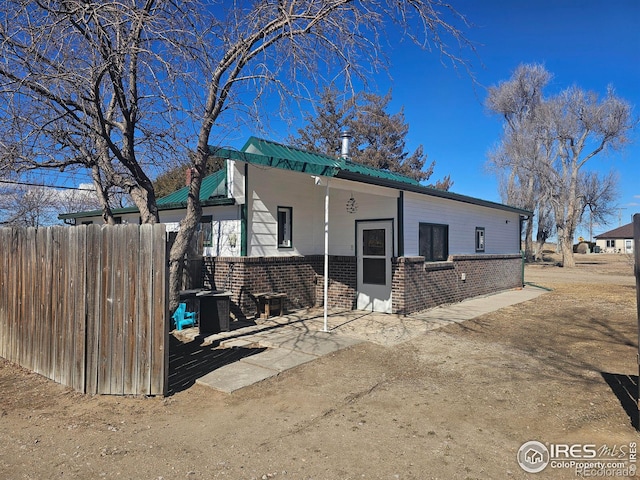 view of front of house featuring a patio area, brick siding, metal roof, and fence